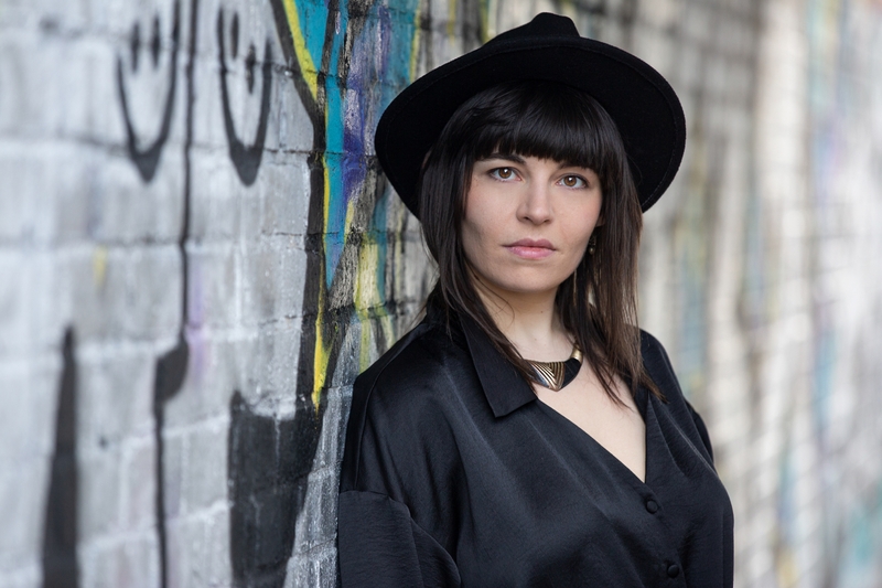 Colour photo of Lara wearing a hat against a graffiti wall - taken by Nick Brittain