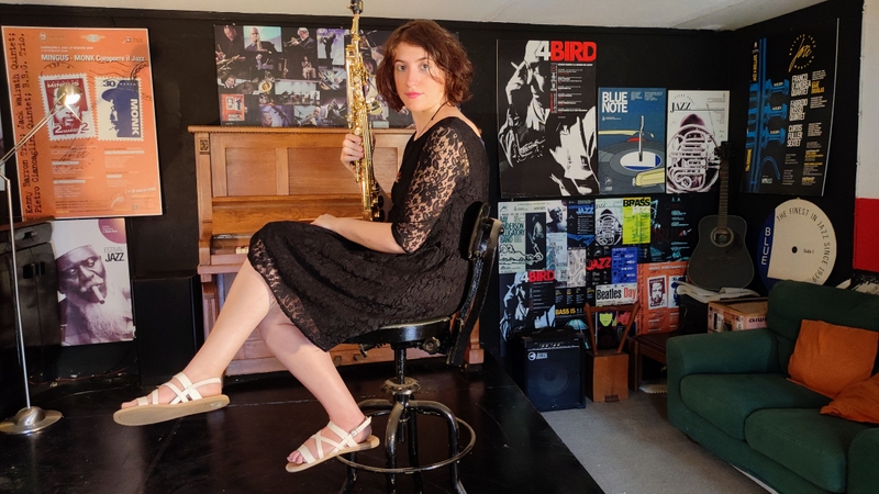 Colour photo of Betty sitting on a chair with her saxophone