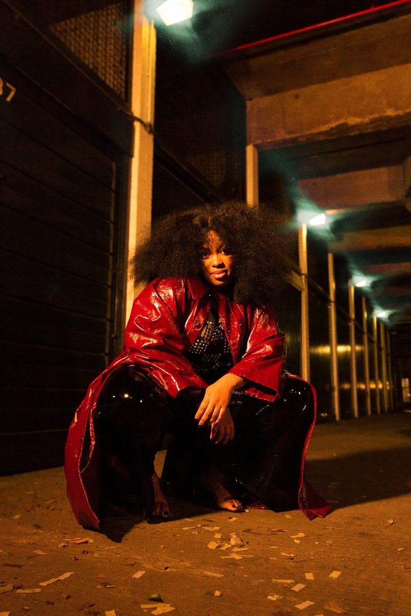 Colour photo of Mary Sho, crouched down in a shiny red raincoat