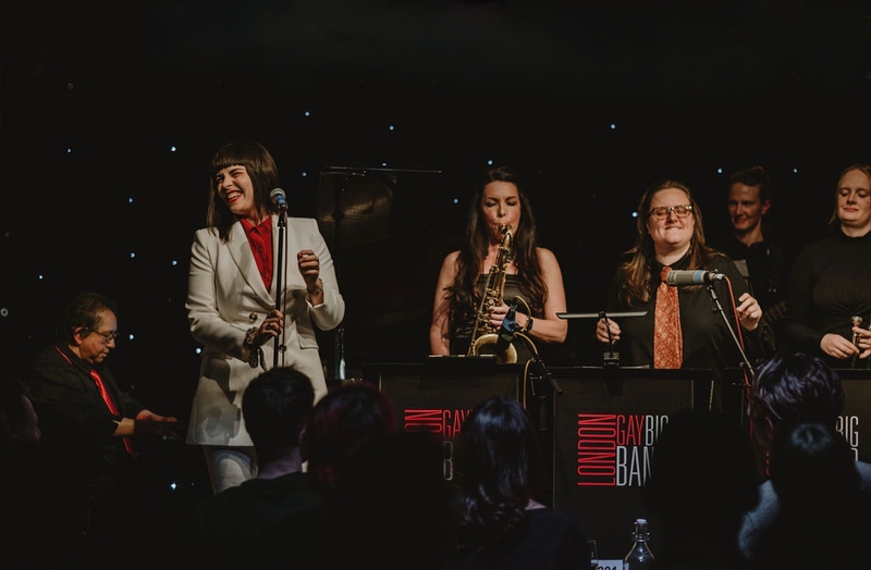 Vibrant photo of the London Gay Big Band performing, everyone smiling - taken by Jess Rose