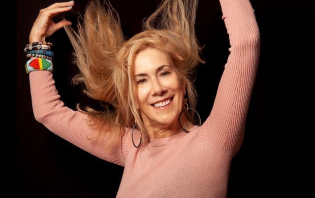 Colour photo of Jane Cornwell in a pink jumper flicking her hair in the air - taken by Lukasz Izdebski